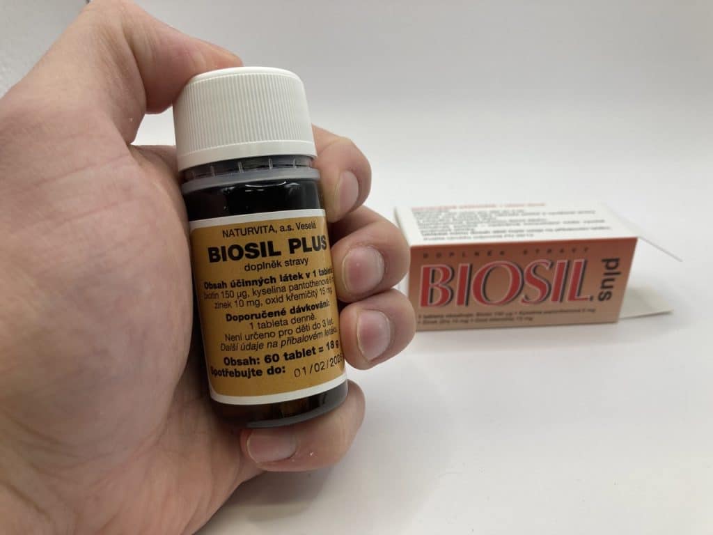 Složení krabičky Biosil Plus. V ruce Biosil balení. Vzadu krabička od balení. Bílé plátno. Foceno na mobil.
